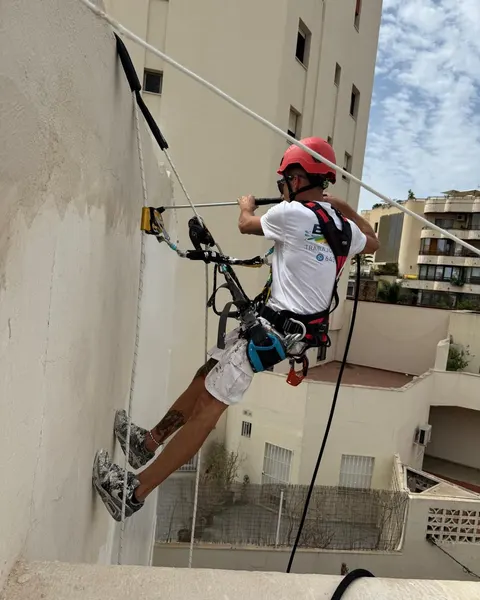 Pintor de Pinturas BNR colgado con cuerdas y arnés en la fachada de un edificio
